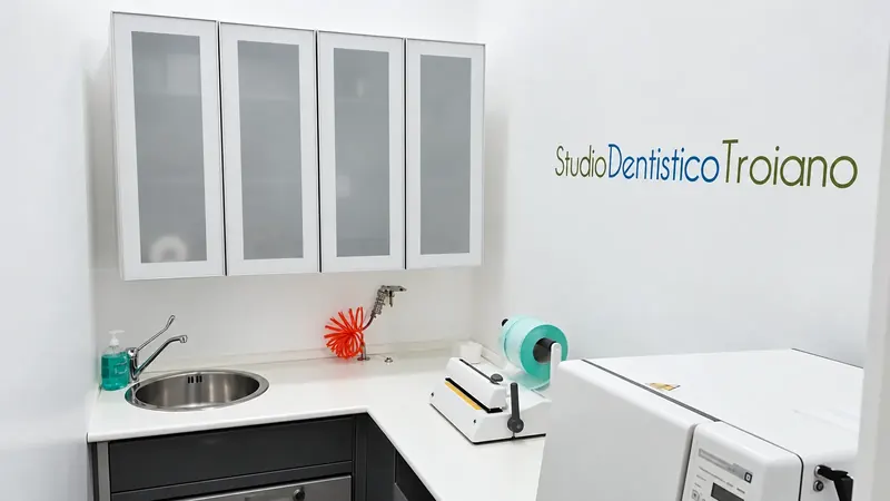 Area di sterilizzazione con pensili bianchi, lavello, imbustatrice e la scritta Studio Dentistico Troiano sulla parete